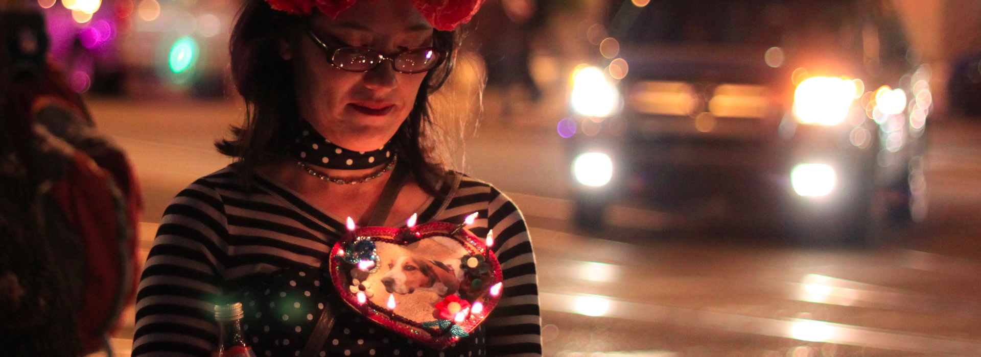 All Souls Attendee with lighted necklace honoring her dog - face illuminated by her cellphone